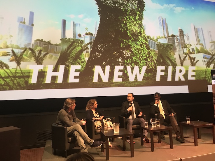 Three men and one woman seated on front of a large image on which The New Fire is printed